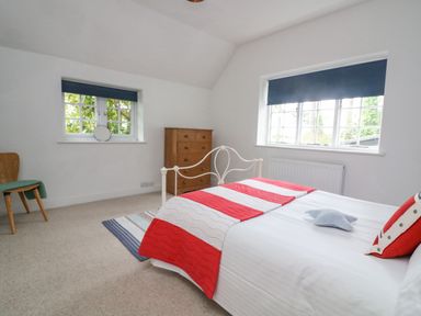 A bedroom with a white metal bed red and white bedding a wooden chest of drawers and two windows with blue blinds at Landmark in Salcombe