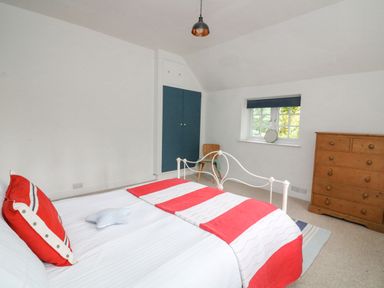 A bedroom with a white metal bed frame red and white bedding a wooden chest of drawers a wooden chair blue closet doors and a small window with a blue blind at Landmark in Salcombe