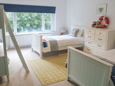 A bedroom with two single beds a bunk bed a chest of drawers and a large window at Landmark in Salcombe