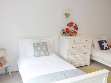 A bedroom with two white beds a white chest of drawers and a small side table with a lamp at Landmark in Salcombe