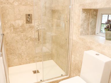 A bathroom with a glass shower enclosure beige tiled walls a white toilet and a small window with a plant at Landmark in Salcombe