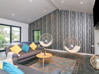 A living room with two hanging bubble chairs a ping pong table and grey sofas with colorful pillows at Landmark in Salcombe