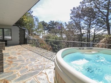 An outdoor patio with a hot tub and wicker furniture overlooking trees at Landmark in Salcombe