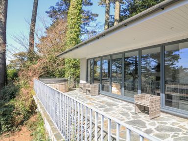An outdoor patio with stone flooring wicker furniture and a hot tub surrounded by trees at Landmark in Salcombe