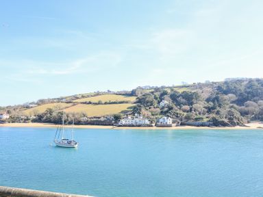 A sailboat on blue water with houses and green hills in the background at Landmark in Salcombe