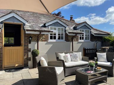 An outdoor seating area with wicker chairs sofa and a glass coffee table in front of a house with a wooden door and three windows at The Coach House at Lackington Farm in Piddletrenthide