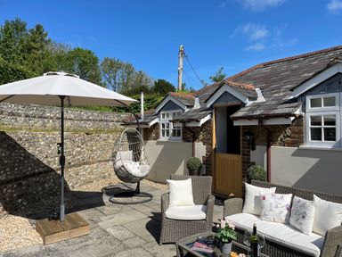 An outdoor patio with wicker chairs and sofa under a large umbrella and a hanging egg chair at The Coach House at Lackington Farm in Piddletrenthide