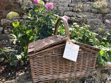 A wicker picnic basket with a note in front of a stone wall and flowers at The Coach House at Lackington Farm in Piddletrenthide