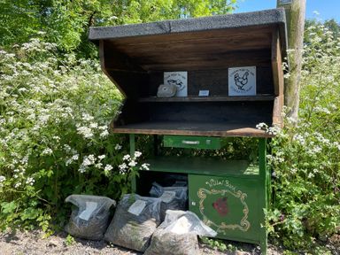 A wooden stand with signs for duck and chicken eggs for sale by the roadside with bags of compost or soil at The Coach House at Lackington Farm in Piddletrenthide