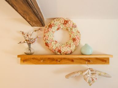 A wooden shelf with a glass vase of flowers a floral wreath a small ceramic vase and a fabric hanger at The Coach House at Lackington Farm in Piddletrenthide