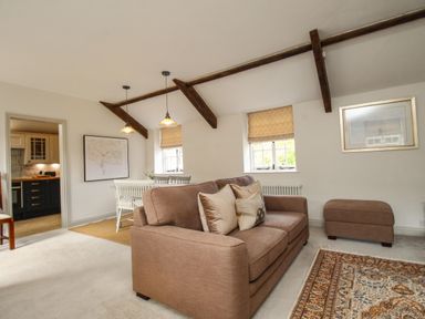 A living room with a brown sofa and ottoman a dining table with white chairs and pendant lights at The Coach House at Lackington Farm in Piddletrenthide