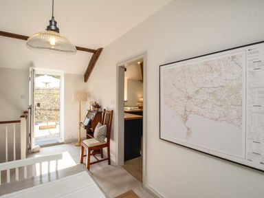 A room with a wooden chair and a small desk near an open door showing an outdoor umbrella and swing at The Coach House at Lackington Farm Piddletrenthide