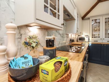 A kitchen countertop with tea packets in a bowl ginger biscuits and jars with cabinets and a microwave in the background at The Coach House at Lackington Farm in Piddletrenthide