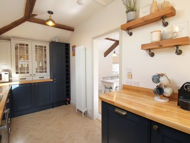 A kitchen with wooden countertops blue cabinets hanging shelves and a doorway leading to a dining area at The Coach House at Lackington Farm in Piddletrenthide
