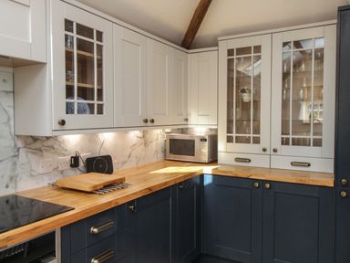 A kitchen with white upper cabinets and dark lower cabinets with wooden countertops and a microwave at The Coach House at Lackington Farm in Piddletrenthide