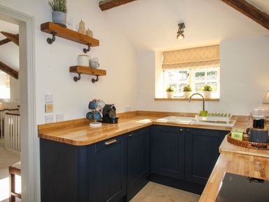 A kitchen with wooden countertops blue cabinets a sink under a window and shelves with cups at The Coach House at Lackington Farm in Piddletrenthide