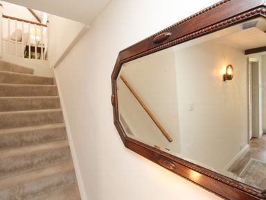 A carpeted staircase with a wooden handrail and an octagonal framed mirror on the wall at The Coach House at Lackington Farm in Piddletrenthide