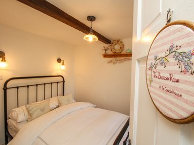 A bedroom with a metal bed frame white bedding wall lights and a wooden shelf with hangers at The Coach House at Lackington Farm Piddletrenthide