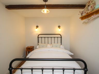 A bedroom with a bed with white bedding a wooden nightstand two wall lamps and a wooden beam across the ceiling at The Coach House at Lackington Farm in Piddletrenthide