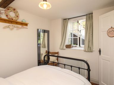 A bedroom with a metal bed frame chair with pillows window with curtains and a mirror at The Coach House at Lackington Farm in Piddletrenthide