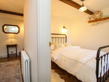 A bedroom with a metal bed frame and white bedding next to a hallway with a wooden table and lamp at The Coach House at Lackington Farm in Piddletrenthide