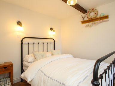 A bedroom with a black metal bed frame white bedding two striped cushions wooden side table and wall lights at The Coach House at Lackington Farm in Piddletrenthide