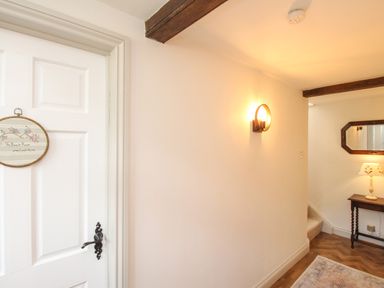 A hallway with a white door and a wall light a wooden table with a lamp and a mirror above it at The Coach House at Lackington Farm in Piddletrenthide