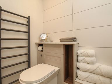 A bathroom with a toilet a towel rack and folded towels on a shelf at The Coach House at Lackington Farm in Piddletrenthide