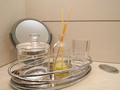 A bathroom countertop with a round mirror a glass jar a reed diffuser and a glass holder at The Coach House at Lackington Farm in Piddletrenthide
