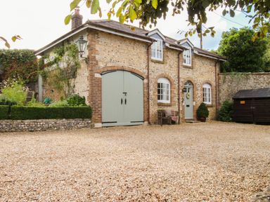 A stone house with green doors and windows with a gravel courtyard at The Coach House at Lackington Farm in Piddletrenthide