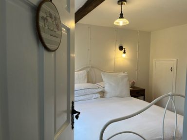 A bedroom with a white metal bedframe pillows bedside table a lamp on the wall and a door sign at The Coach House at Lackington Farm Piddletrenthide