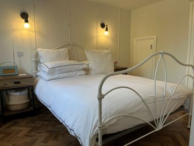 A bedroom with a white metal bed frame white bedding and pillows two wall lights and wooden side tables at The Coach House at Lackington Farm in Piddletrenthide