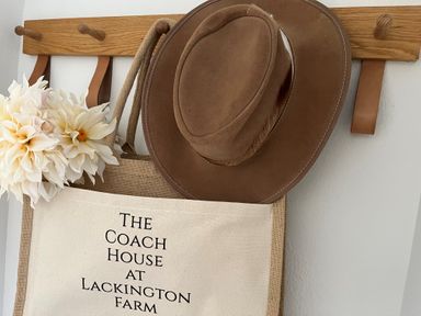 A wall-mounted wooden coat rack holding a hat, flowers, and a bag with text in a hallway at The Coach House at Lackington Farm Piddletrenthide