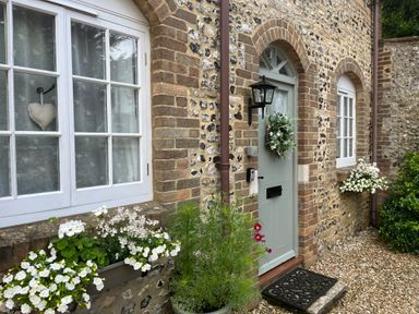 A stone and brick house facade with white windows flower boxes and a green door with a wreath at The Coach House at Lackington Farm Piddletrenthide