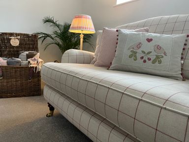 A checkered sofa with cushions and a floor lamp beside a wicker basket with blankets and a plant in a living room at The Coach House at Lackington Farm in Piddletrenthide