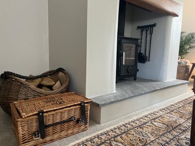 A fireplace with a black wood stove a basket of firewood and a wicker basket on a carpeted floor at The Coach House at Lackington Farm in Piddletrenthide