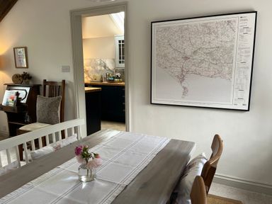 A dining room with a wooden table and chairs a small vase with flowers a map on the wall and a doorway leading to a kitchen at The Coach House at Lackington Farm in Piddletrenthide