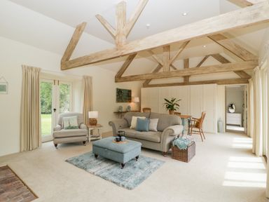 A living room with a sofa armchair ottoman rug dining table chairs and exposed wooden beams at The Shippon in Honiton
