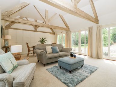A living room with exposed wooden beams a sofa armchair ottoman and large windows at The Shippon in Honiton