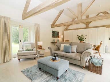 A living room with sofa armchair ottoman and wooden beams at The Shippon in Honiton