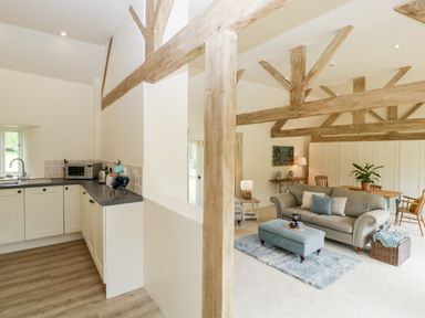 A kitchen area with white cabinets and a living room with a sofa ottoman and dining table at The Shippon in Honiton
