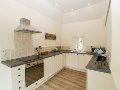 A kitchen with white cabinets black countertops a stove oven a microwave and a small window at The Shippon in Honiton