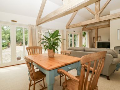 A dining area with a wooden table and four chairs and a living area with a sofa and television at The Shippon in Honiton