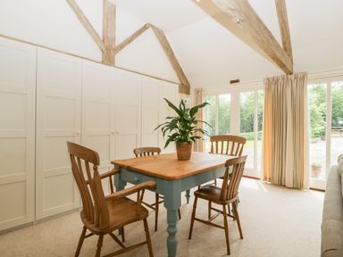 A dining area with wooden chairs and table featuring a plant in a pot near large windows and built-in cupboards at The Shippon in Honiton