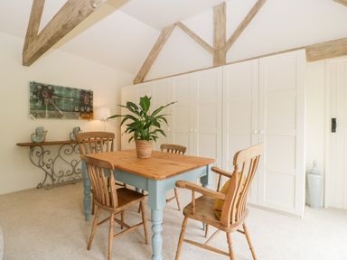 A dining area with a wooden table and four chairs a potted plant on the table a side table with decorative items and a painting on the wall at The Shippon in Honiton