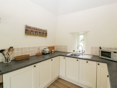 A kitchen with white cabinets a black countertop a sink a microwave and kitchen utensils at The Shippon in Honiton
