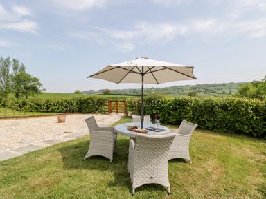 An outdoor patio area with a round table and four chairs under a large umbrella with a wine bottle and glasses on the table at The Shippon in Honiton