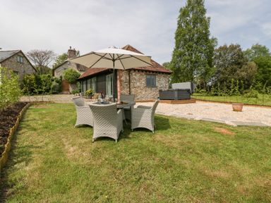 A garden with a table and four chairs under an umbrella next to a stone house at The Shippon in Honiton