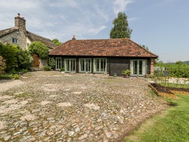 A courtyard with cobblestone paving and a building with multiple windows at The Shippon in Honiton