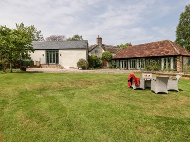 A large green lawn with outdoor table and chairs and three buildings in the background at The Shippon in Honiton